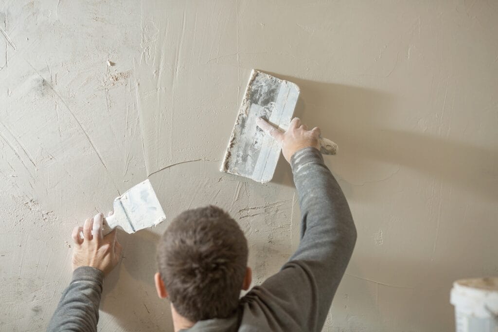 a man stands at a rough plastered wall with spatulas.