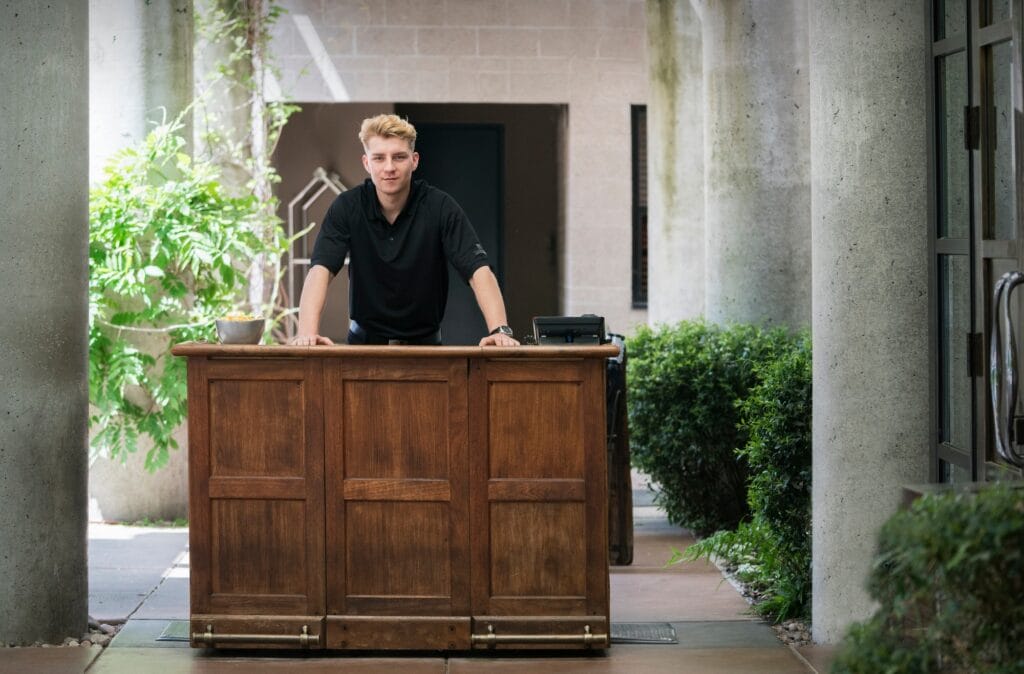 Bellhop standing at wooden reception desk of a downtown hotel.