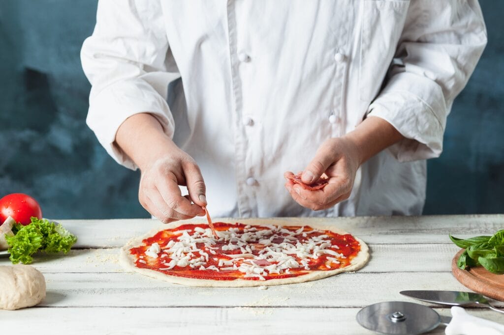 Closeup hand of chef baker in white uniform making pizza at kitchen