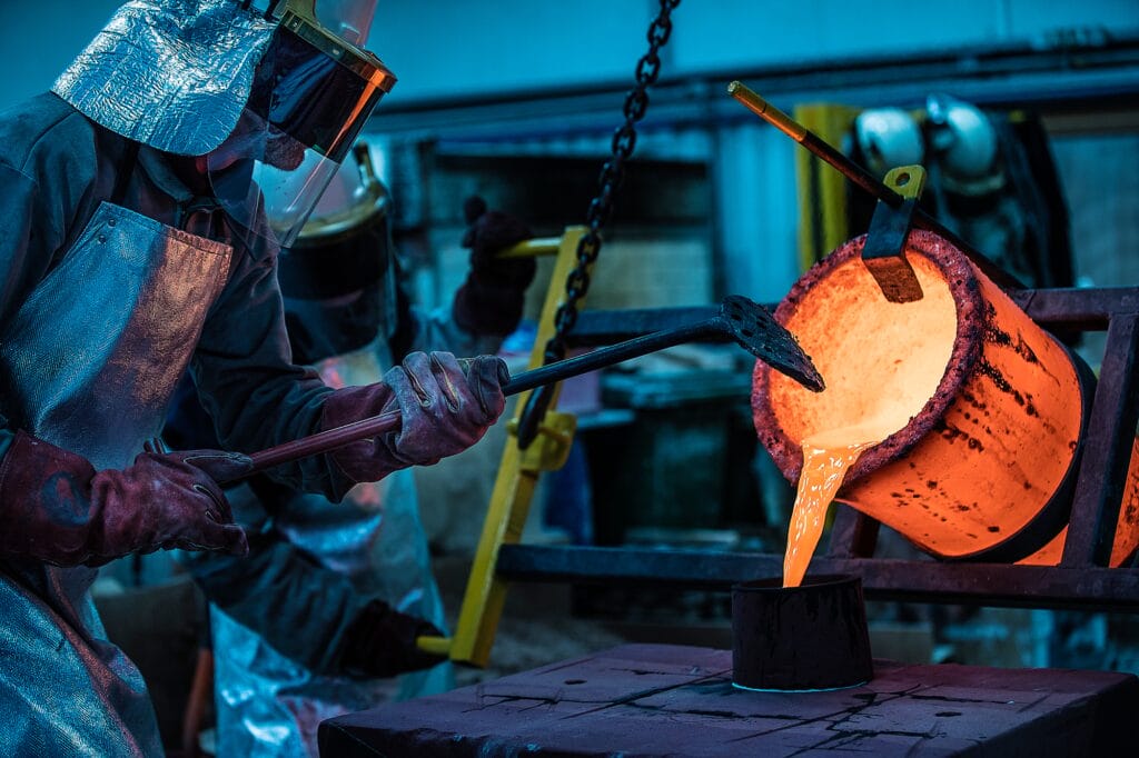 Male foundry workers pouring bronze melting pot in bronze foundry