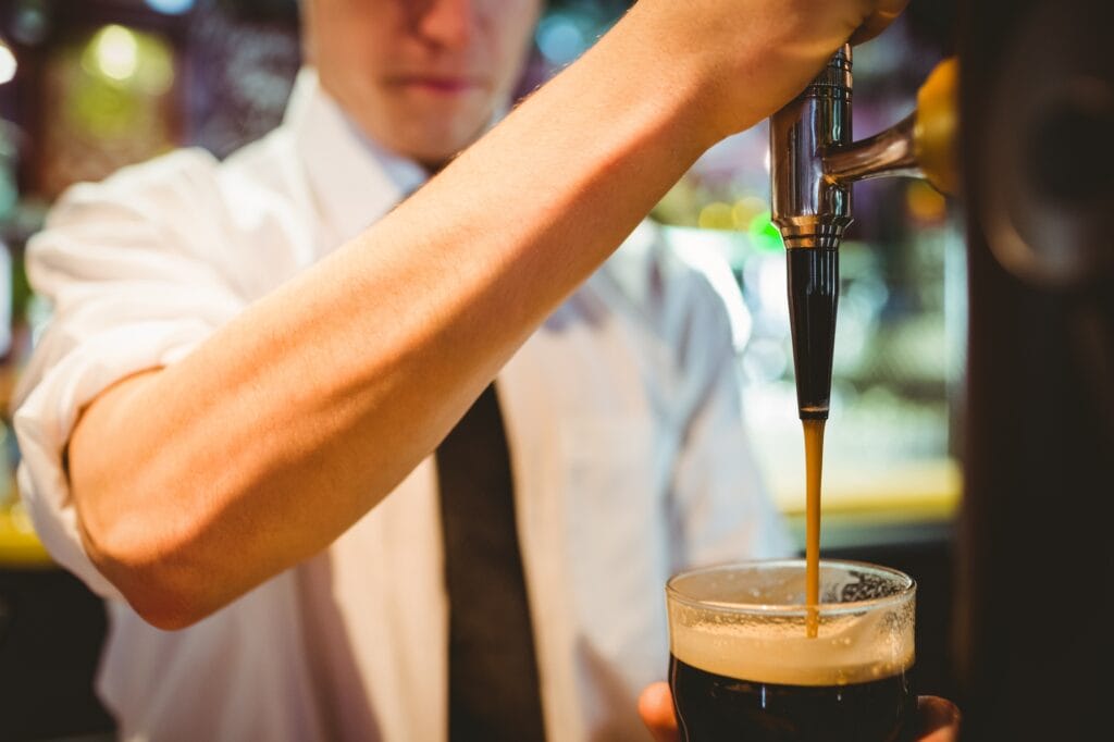 Mid section of barkeeper holding beer glass below dispenser tap at bar counter