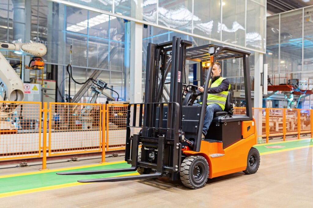 Storehouse employee in uniform working on forklift in modern factory with robots and manipulators