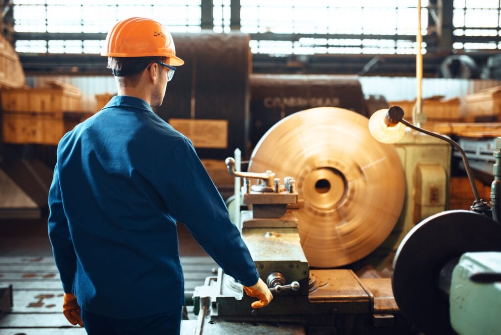 Turner in uniform and helmet works on lathe