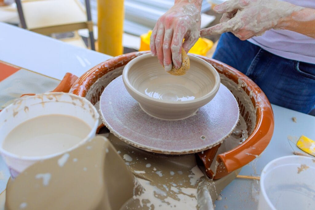 Using wet hands, ceramicist shapes soft clay on a potter wheel