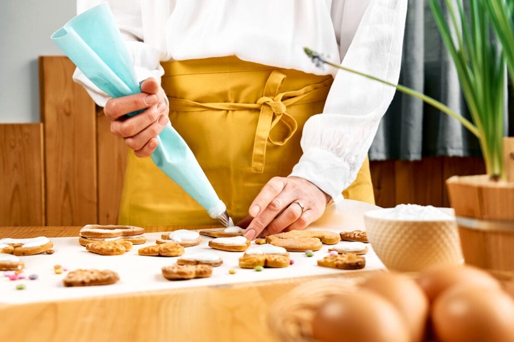 Woman decorating heart shaped cookies with frosting. Glazed festive homemade biscuits