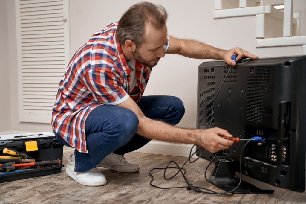Young caucasian repairman mending tv receiver with screwdriver