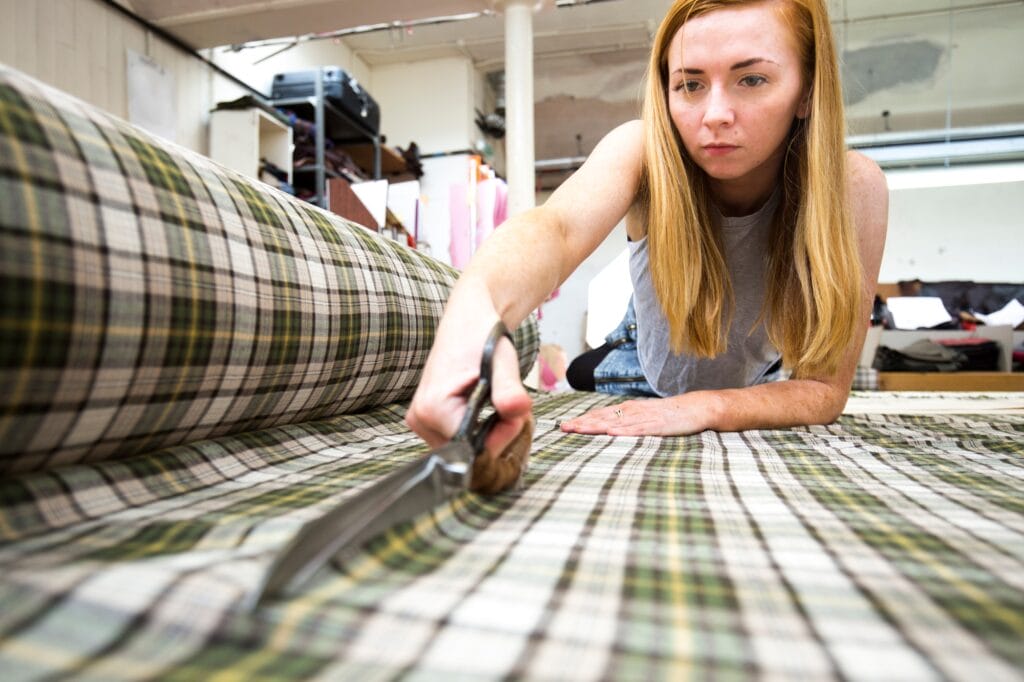 Young woman cutting fabric in leather jacket manufacturers